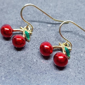 Puede incluir: Un par de pendientes de cereza de oro con cerezas rojas y hojas verdes.