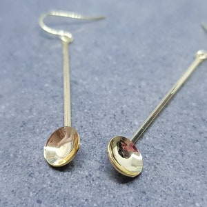 Op de afbeelding: Een paar gouden oorhangers met een ronde, licht concave schijf aan het einde van elke oorhanger.