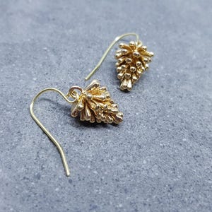 May include: A pair of gold dangle earrings with a textured, spiky design. The earrings are made of metal and have a simple, minimalist style.