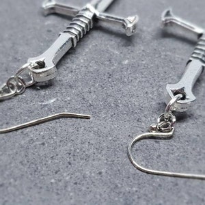 Peut inclure: Une paire de boucles d'oreilles en forme d'&eacute;p&eacute;e argent&eacute;es avec un design d&eacute;taill&eacute;. Les boucles d'oreilles ont une fermeture &agrave; crochet.