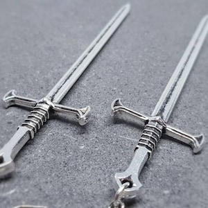 Peut inclure: Une paire de boucles d'oreilles en forme d'&eacute;p&eacute;e argent&eacute;e. Les &eacute;p&eacute;es ont un design d&eacute;taill&eacute; avec une poign&eacute;e torsad&eacute;e et une pointe pointue.