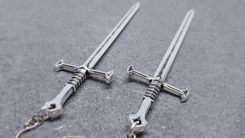 Peut inclure: Une paire de boucles d'oreilles en forme d'&eacute;p&eacute;e argent&eacute;e. Les &eacute;p&eacute;es ont un design d&eacute;taill&eacute; avec une poign&eacute;e torsad&eacute;e et une pointe pointue.