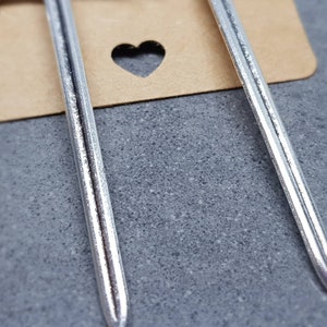Peut inclure: Deux boucles d'oreilles en forme d'&eacute;p&eacute;e argent&eacute;es avec une surface textur&eacute;e.