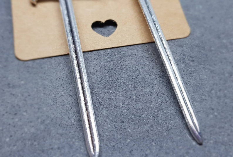 Peut inclure: Deux boucles d'oreilles en forme d'&eacute;p&eacute;e argent&eacute;es avec une surface textur&eacute;e.