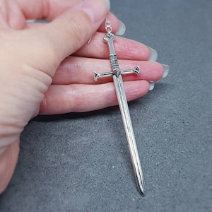 Peut inclure: Boucle d'oreille pendante en forme d'&eacute;p&eacute;e argent&eacute;e. L'&eacute;p&eacute;e a un design d&eacute;taill&eacute; avec une pointe pointue et une garde crois&eacute;e.