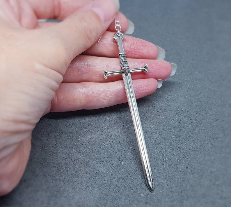Peut inclure: Boucle d'oreille pendante en forme d'&eacute;p&eacute;e argent&eacute;e. L'&eacute;p&eacute;e a un design d&eacute;taill&eacute; avec une pointe pointue et une garde crois&eacute;e.