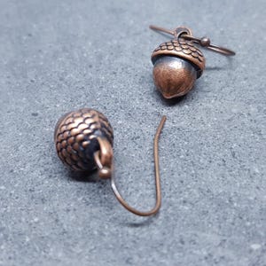 May include: A pair of copper acorn earrings with a textured finish. The earrings are on a grey background.