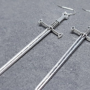 Peut inclure: Une paire de boucles d'oreilles en forme d'&eacute;p&eacute;e argent&eacute;es. Les &eacute;p&eacute;es sont d&eacute;taill&eacute;es avec une finition textur&eacute;e et ont une pointe pointue.