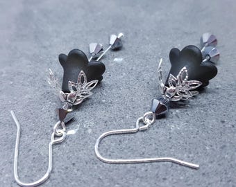 May include: A pair of black flower-shaped earrings with silver-colored filigree accents and dangling silver-colored hooks. The earrings have small, faceted gray beads and are set against a gray background.