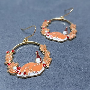 May include: Gold-tone hoop earrings featuring a Thanksgiving theme. Each earring showcases a roasted turkey, a wine bottle, and a wreath of autumn leaves and berries. The earrings have a festive, enamel-like finish.