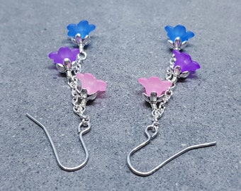 Könnte beinhalten: Ein Paar silberne Ohrringe mit einer Kette und vier blütenförmigen Anhängern. Die Anhänger sind blau, lila und rosa.