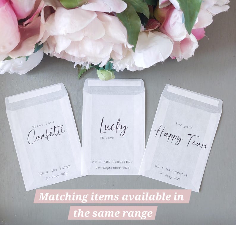 May include: Three translucent white paper envelopes with black printed text. The first reads Throw some Confetti, Mr & Mrs Smith, 9th July 2026. The second reads Lucky in love, Mr & Mrs Schofield, 22nd September 2026. The third reads For your Happy Tears, Mr & Mrs Keates, 7th July 2027.