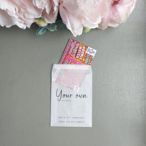 May include: A translucent white paper envelope featuring the black printed text Your own wording, AMY'S 30TH BIRTHDAY, and Thank you for coming. A pink and orange Double Match scratch card with a 5,000 pound top prize is partially inserted inside.
