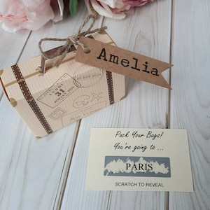 A vintage style beige and brown cardboard suitcase with brown handle and a personalised luggage name tag which is attached by twine. Inside the suitcase fits the scratch and reveal destination card  which can be personalised with the destination