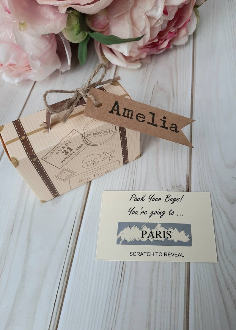 A vintage style beige and brown cardboard suitcase with brown handle and a personalised luggage name tag which is attached by twine. Inside the suitcase fits the scratch and reveal destination card  which can be personalised with the destination