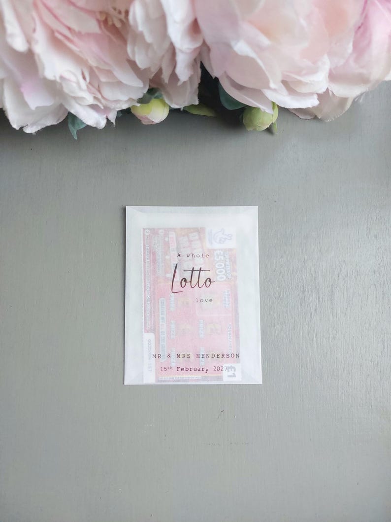May include: A rectangular white translucent paper envelope containing a lottery ticket. The front is printed with the text A whole Lotto love, MR & MRS HENDERSON, and 15th February 2027 in black ink. The ticket inside is visible through the paper.