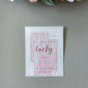 May include: A rectangular white translucent paper envelope containing a pink lottery scratch card. The front of the envelope features black printed text that reads: We hope you get lucky tonight, MR & MRS DEANE, 30th May 2026.