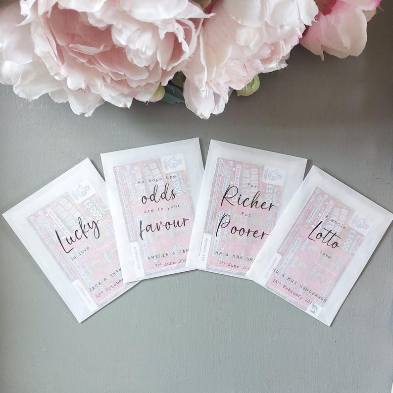 May include: Four white translucent envelopes containing pink lottery tickets. Each envelope features black cursive text: Lucky in love, We hope the odds are in your favour, For Richer For Poorer, and A whole lotto love, with names and dates printed below.