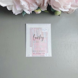 May include: A rectangular translucent paper envelope containing a lottery ticket. The front of the envelope features the black printed text Lucky in love, followed by the names Jack & Shannon and the date 30th October 2026 in a typewriter font.