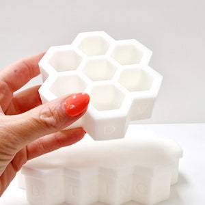 May include: White honeycomb-shaped storage box with a lid. The lid has six compartments shaped like hexagons. The base of the box has the word "DITING" embossed on it.