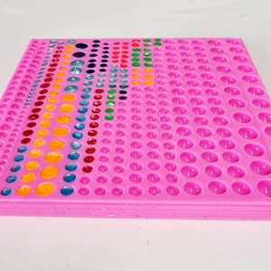 Può includere: Stampo in silicone rosa con più cavità rotonde di diverse dimensioni. Lo stampo è riempito con resina colorata, creando un effetto arcobaleno.