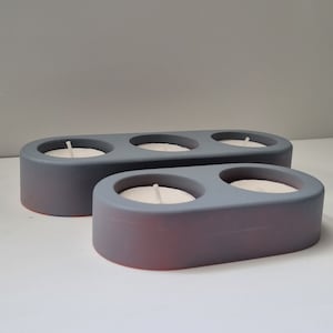 May include: Two gray ceramic candle holders with three candle wells. The top holder has two wells and the bottom holder has one well. The candle holders are oval shaped.