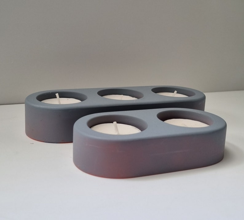 May include: Two gray ceramic candle holders with three candle wells. The top holder has two wells and the bottom holder has one well. The candle holders are oval shaped.