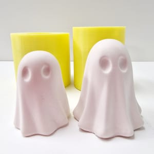 May include: Two pink ghost-shaped silicone moulds for making candles or soap. The moulds are sitting on a white surface next to two yellow silicone moulds.