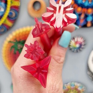 May include: Four red plastic stamps with different floral designs. The stamps are held in a hand.