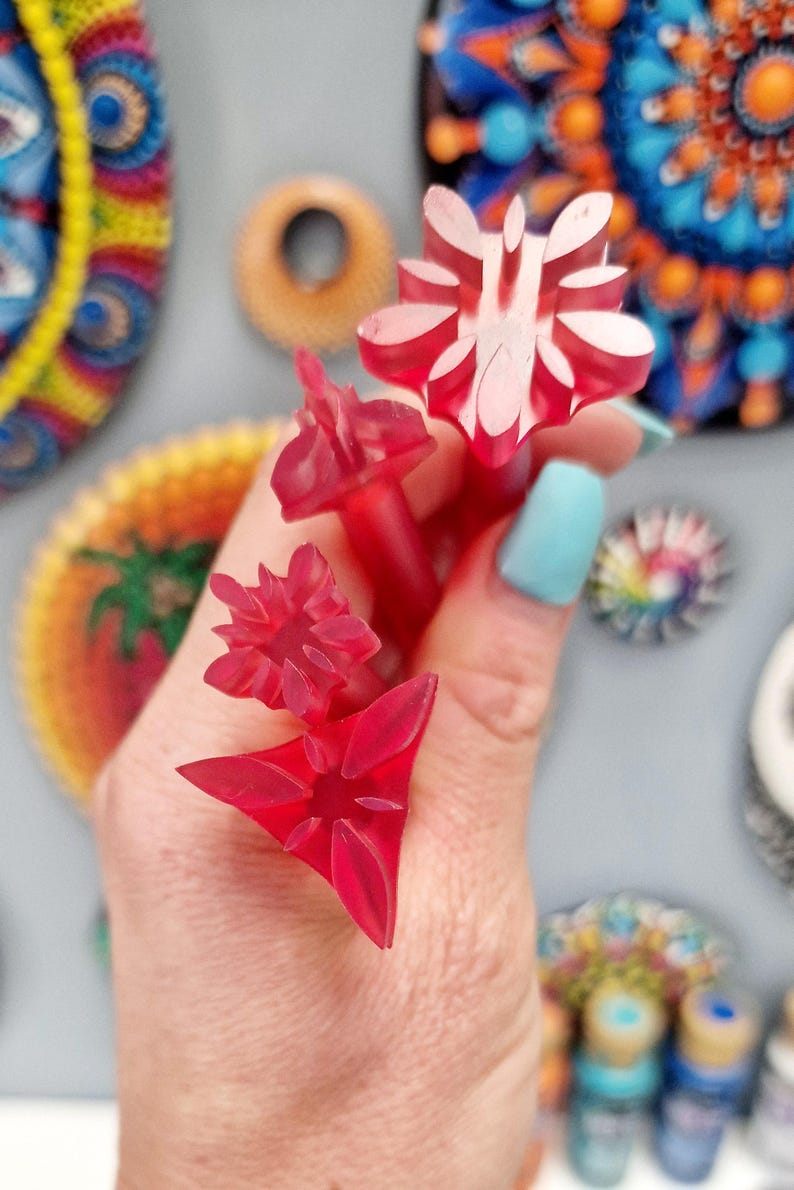 May include: Four red plastic stamps with different floral designs. The stamps are held in a hand.