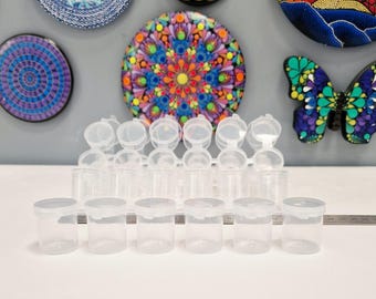 May include: A collection of small, clear plastic containers with hinged lids. The containers are cylindrical and arranged in rows. The lids are white and snap shut. The background features colorful decorative wall art.