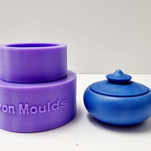 Puede incluir: Un juego de moldes morados con el texto "Devon Moulds" y un recipiente azul con tapa. El juego de moldes incluye dos piezas cilíndricas, una apilada sobre la otra. El recipiente azul tiene una forma redondeada con una tapa pequeña y redondeada.