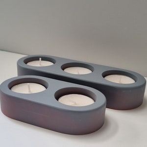 May include: Two gray ceramic candle holders with three and two candle wells. The candle holders are oval shaped and have a matte finish.