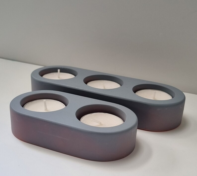 May include: Two gray ceramic candle holders with three and two candle wells. The candle holders are oval shaped and have a matte finish.