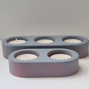 May include: Two gray ceramic candle holders with three and two candle wells. The holders are oval shaped and have a smooth, matte finish.