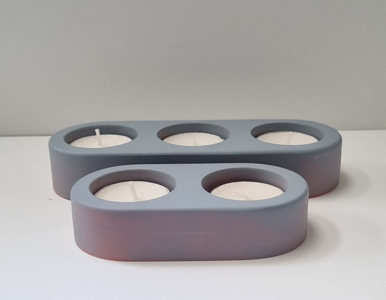 May include: Two gray ceramic candle holders with three and two candle wells. The holders are oval shaped and have a smooth, matte finish.