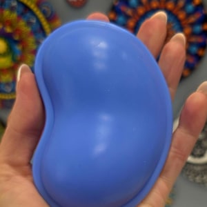 May include: A smooth, solid blue silicone mould shaped like a kidney bean. The object features a rounded, convex surface with a raised outer rim, providing a flexible and durable structure for casting or crafting purposes with a matte finish.