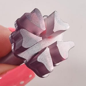 May include: Close-up of a purple metal tool head with a starburst design. The tool head has a series of triangular, petal-like shapes arranged around a central point. The tool is held against a light background.
