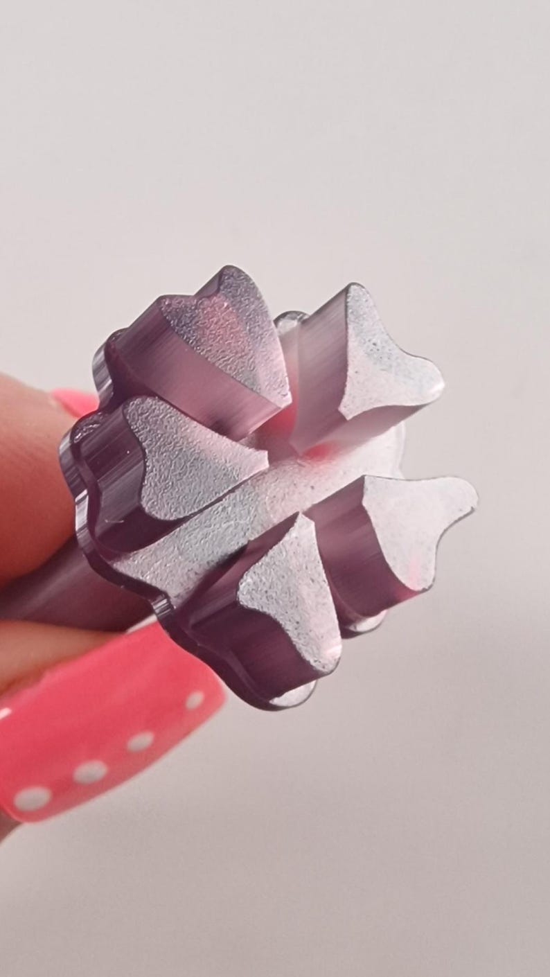 May include: Close-up of a purple metal tool head with a starburst design. The tool head has a series of triangular, petal-like shapes arranged around a central point. The tool is held against a light background.