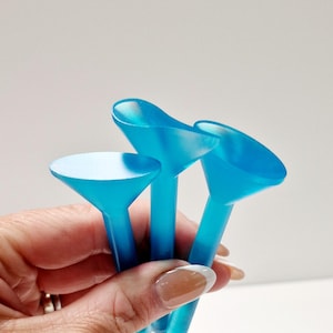 Op de afbeelding: Drie blauwe plastic spuitzaktips met een afgerond, uitlopend uiteinde. De tips worden in een hand gehouden.