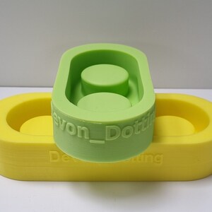 May include: Two silicone molds for making resin crafts. The top mold is green and has two circular depressions. The bottom mold is yellow and has one circular depression. The green mold has the text "Devon_Dotting" on the side.