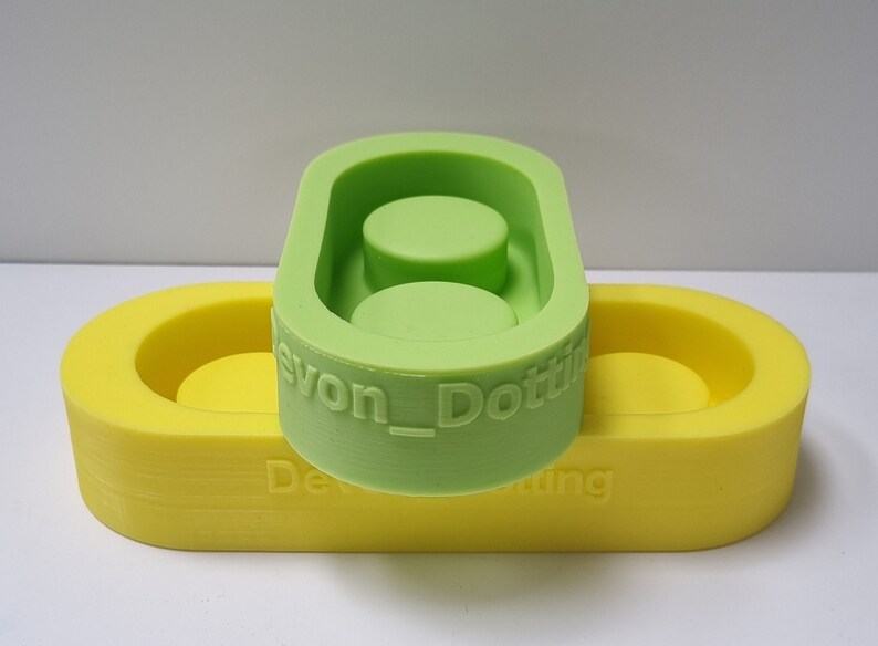 May include: Two silicone molds for making resin crafts. The top mold is green and has two circular depressions. The bottom mold is yellow and has one circular depression. The green mold has the text "Devon_Dotting" on the side.