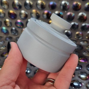 May include: A silver-colored bottle stopper with a rounded top and a smooth, matte finish.
