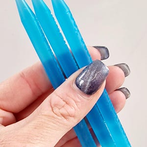 以下が含まれることがあります： 3つの青い、尖ったネイルアートツールが手に持たれています。ツールは鮮やかで半透明の青色で、鋭い円錐形の先端が付いています。これらのツールは、詳細なネイルアートアプリケーション向けに設計されています。