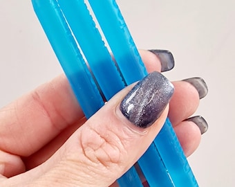 May include: Three blue, pointed nail art tools are held in a hand. The tools are a vibrant, translucent blue, with a sharp, conical tip. The tools are designed for detailed nail art applications.