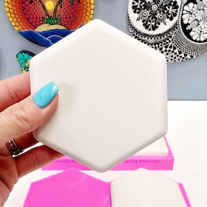 Puede incluir: Un molde de silicona rosa con dos cavidades hexagonales para hacer arte de resina. El molde está etiquetado como "Devon Dotz" y "Dotz Sisters".