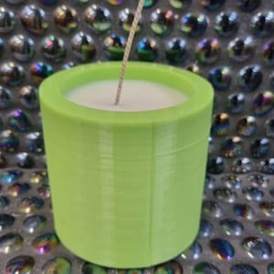 May include: A green cylindrical candle container with a white candle and a wick inside. The container has a textured surface.