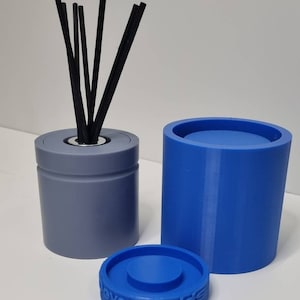 May include: A set of two blue silicone moulds for making diffuser bottles. The smaller mould has a groove around the middle and the larger mould is taller. The moulds are on a white surface. The smaller mould has black diffuser sticks in it.