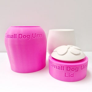 May include: A pink small dog urn with a white lid. The lid has a paw print design and the words "Small Dog Urn Lid" are embossed on the side.
