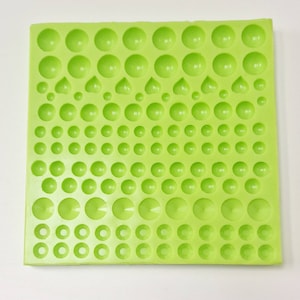 May include: A green silicone mould with multiple round and heart-shaped cavities of varying sizes. The mould is designed for creating decorative embellishments.